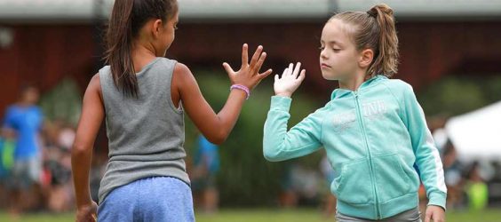 two female children on a sports field with their hands up about to high five