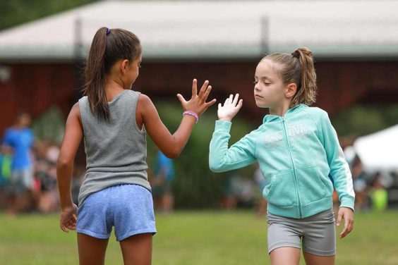 two female children on a sports field with their hands up about to high five