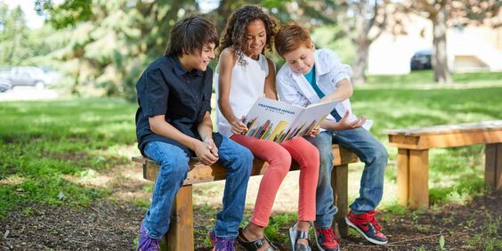 three kids sitting on a bench looking at their yearbook